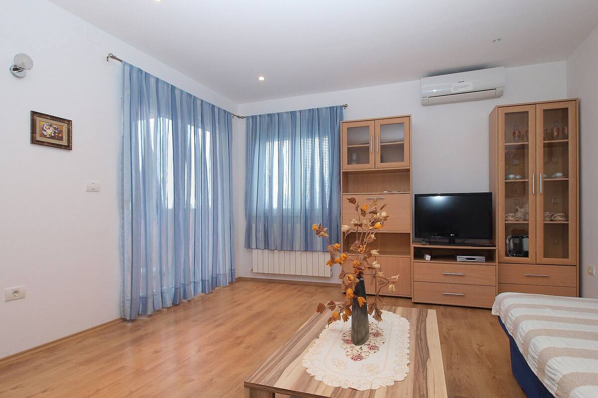 A modern living room with a wooden floor, a TV, a cabinet, and a vase with dried flowers on a table.