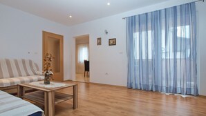 A spacious living room with a striped sofa, a wooden coffee table, and a large window with sheer curtains. - Apartment Mirsad 1282 (Fazana)