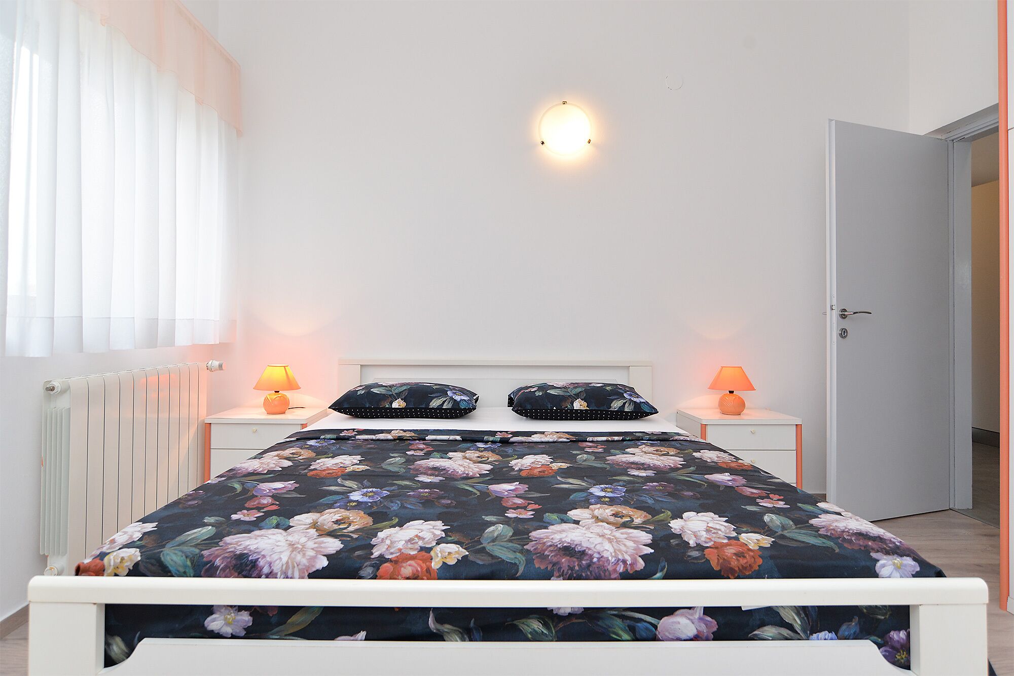 Une chambre à coucher comprenant un lit, deux tables de chevet, une lampe fixée au mur et un radiateur.