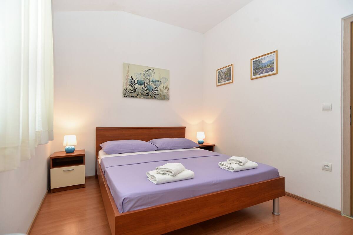 Un lit bien fait, avec une tête de lit en bois, deux tables de chevet avec des lampes et deux tableaux encadrés accrochés au mur.