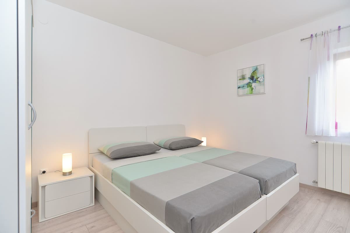 Une chambre à coucher comprenant un lit, des tables de chevet, une commode, une œuvre d’art accrochée au mur et une fenêtre avec des rideaux.