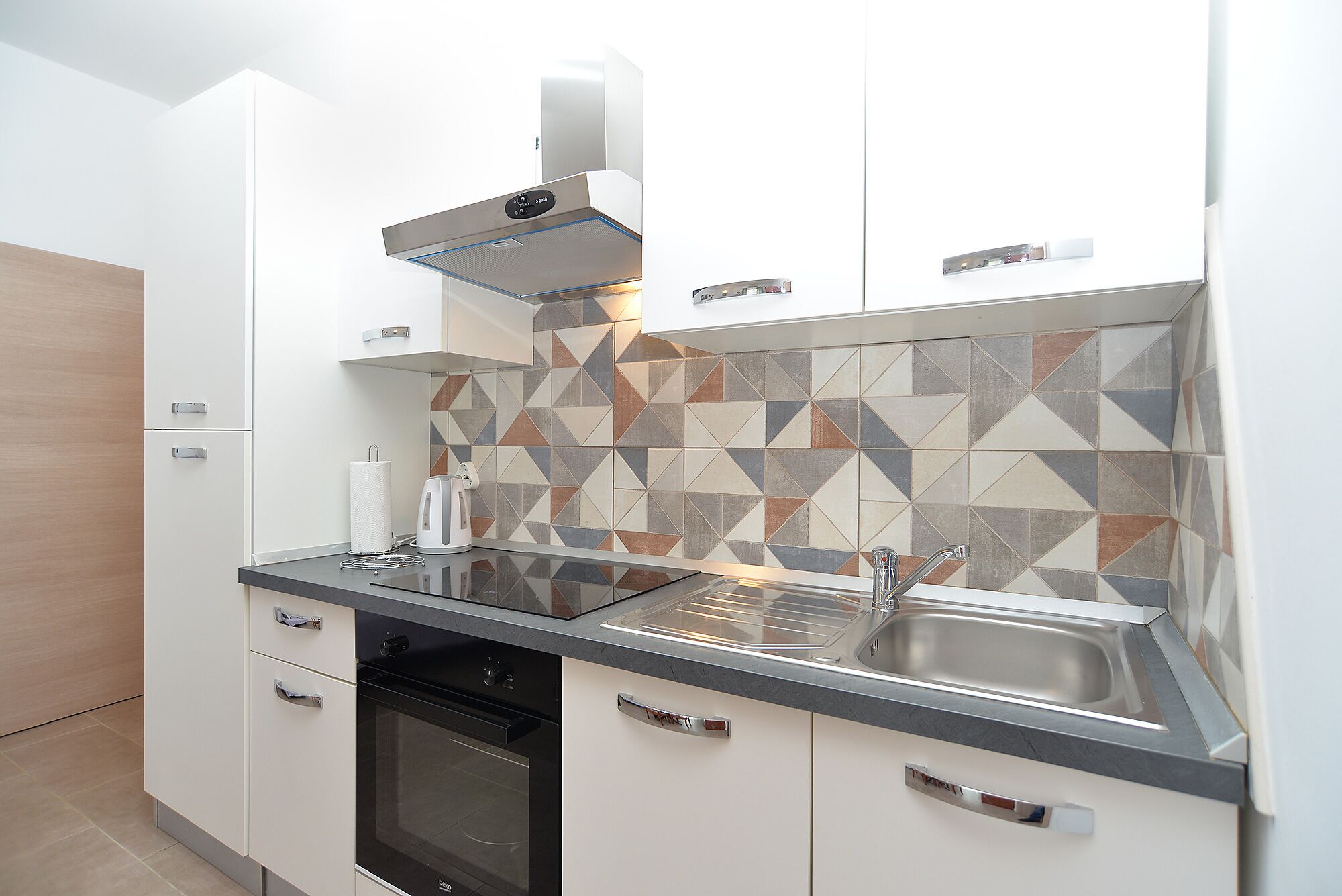 Een moderne keuken met witte kastjes, een zwarte oven, een roestvrijstalen spoelbak en een decoratieve spatwand.