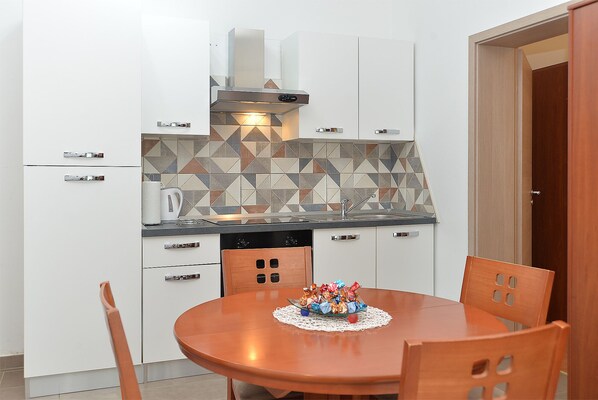 Una cocina compacta con armarios blancos, un salpicadero con diseño y un comedor con mesa y sillas de madera.