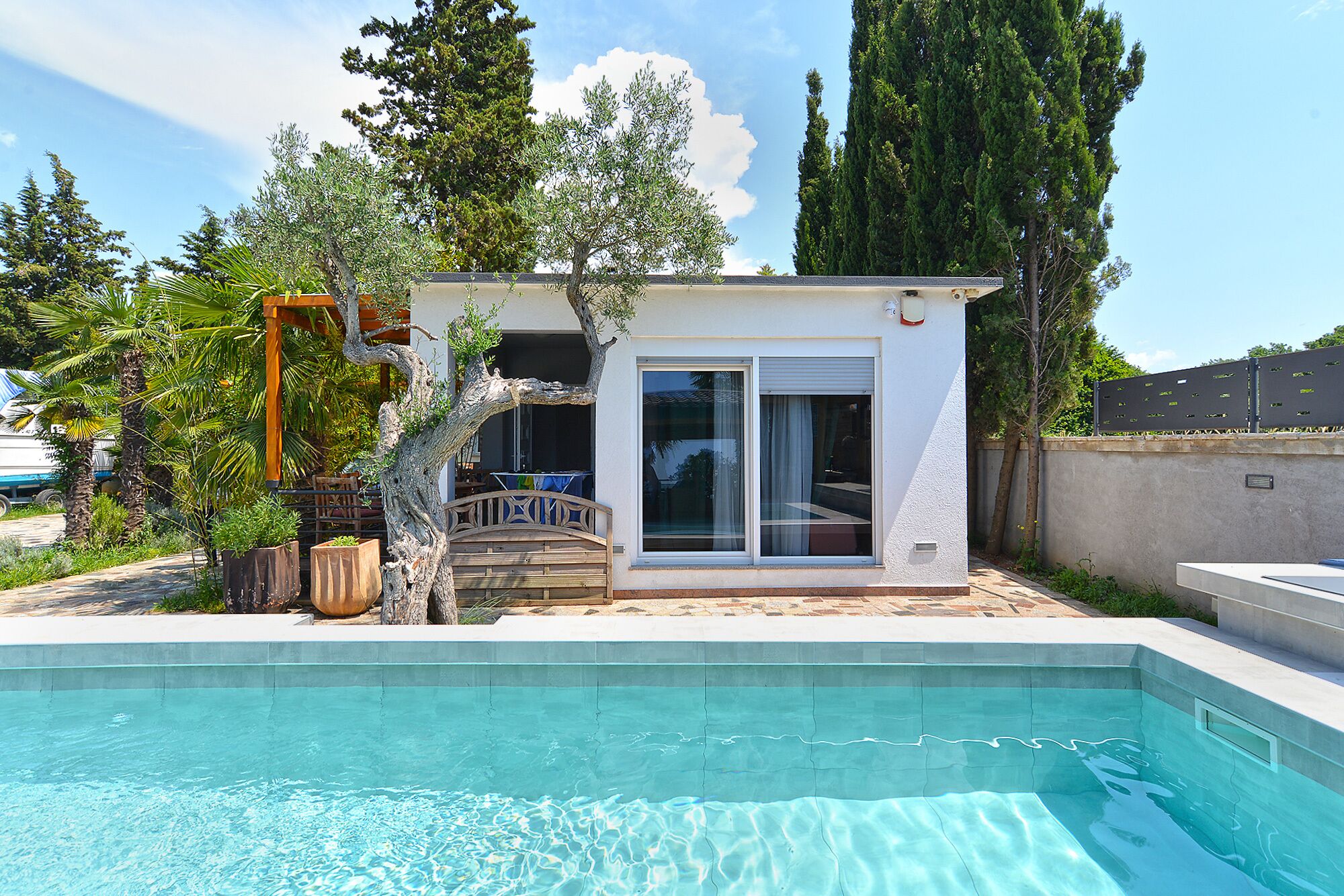 A small building with a pool, surrounded by trees and a clear sky.