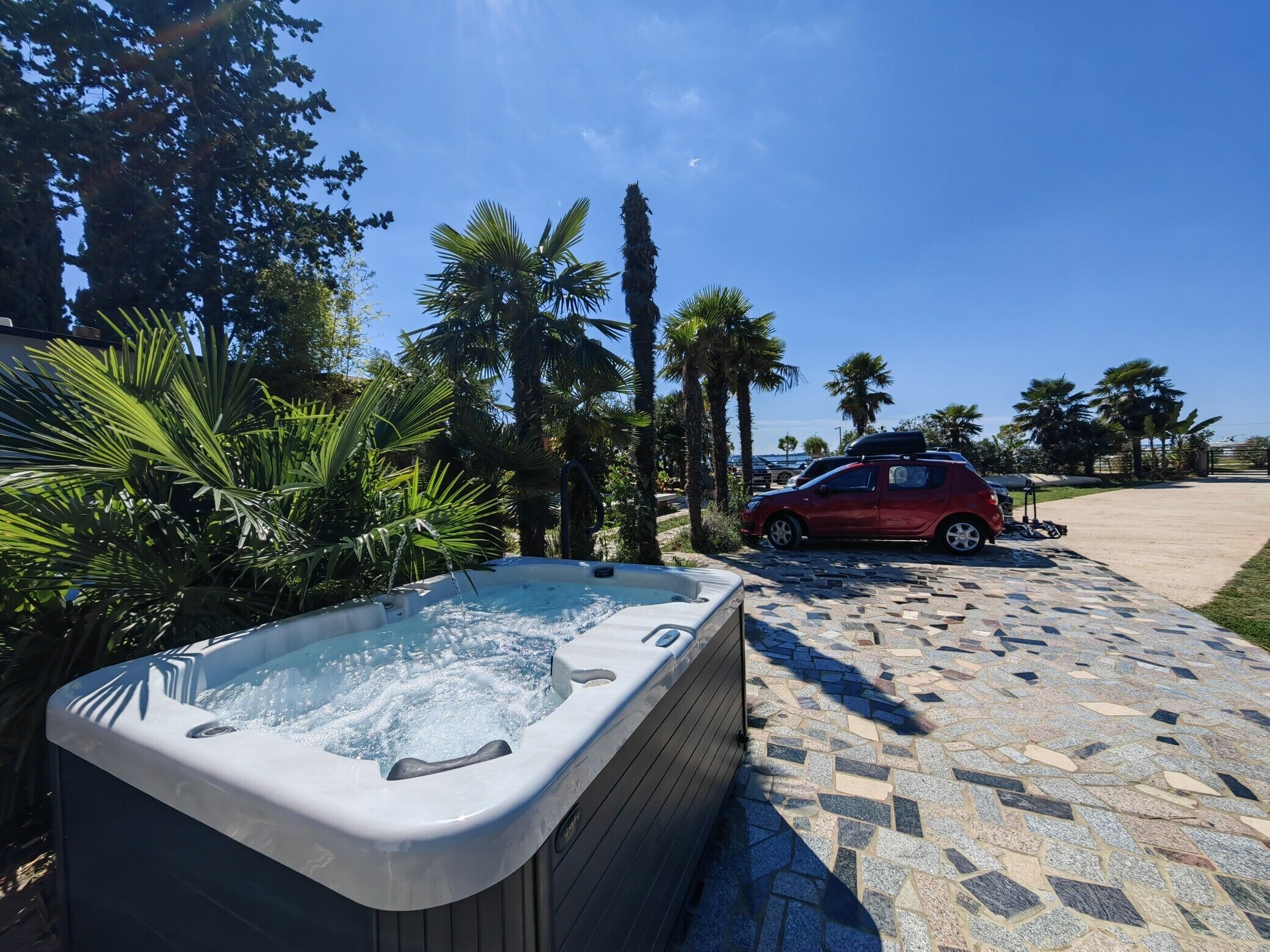 Ein Whirlpool in einem Garten mit Palmen und ein rotes Auto in der Nähe.