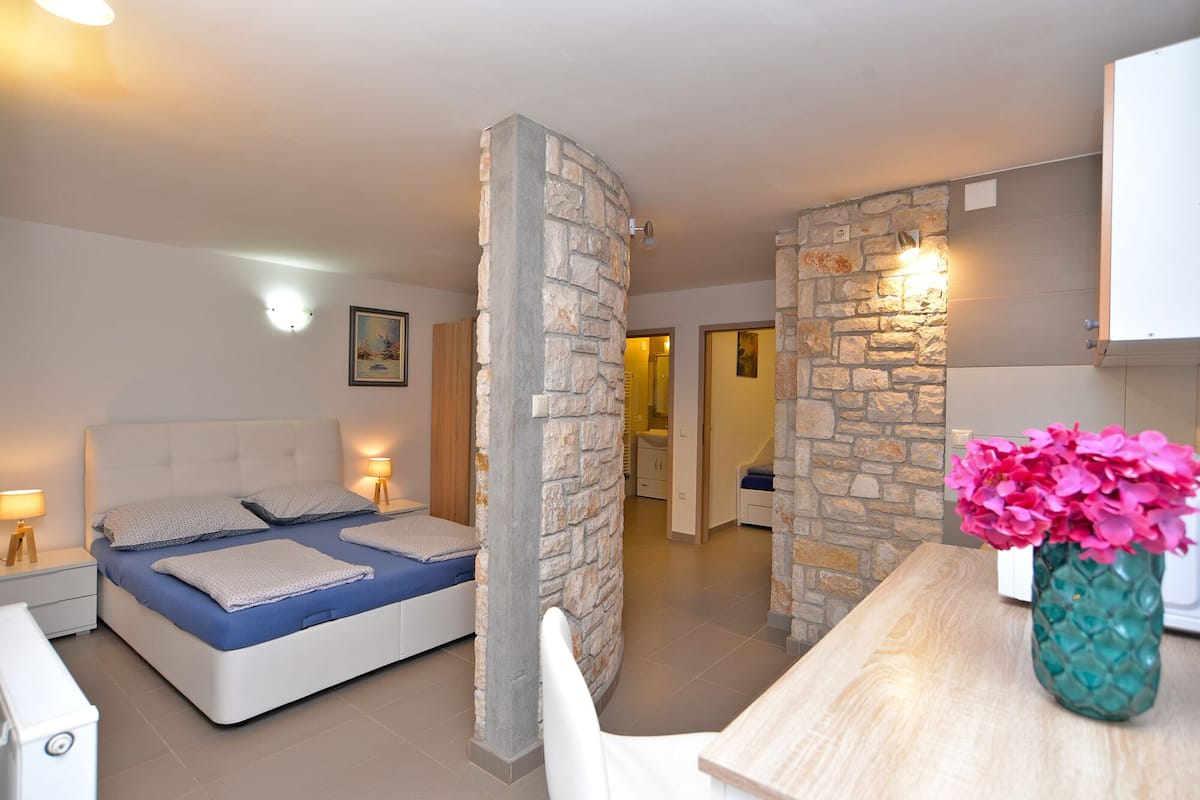 Un dormitorio con cama, mesitas de noche, una mesita auxiliar, una mesa de madera y un jarrón con flores.