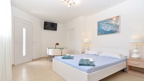 A hotel room with a bed, bedside tables, a desk with a chair, a TV mounted on the wall, and a painting of a cityscape. - Apartment Vlado 1405 (Vodnjan)