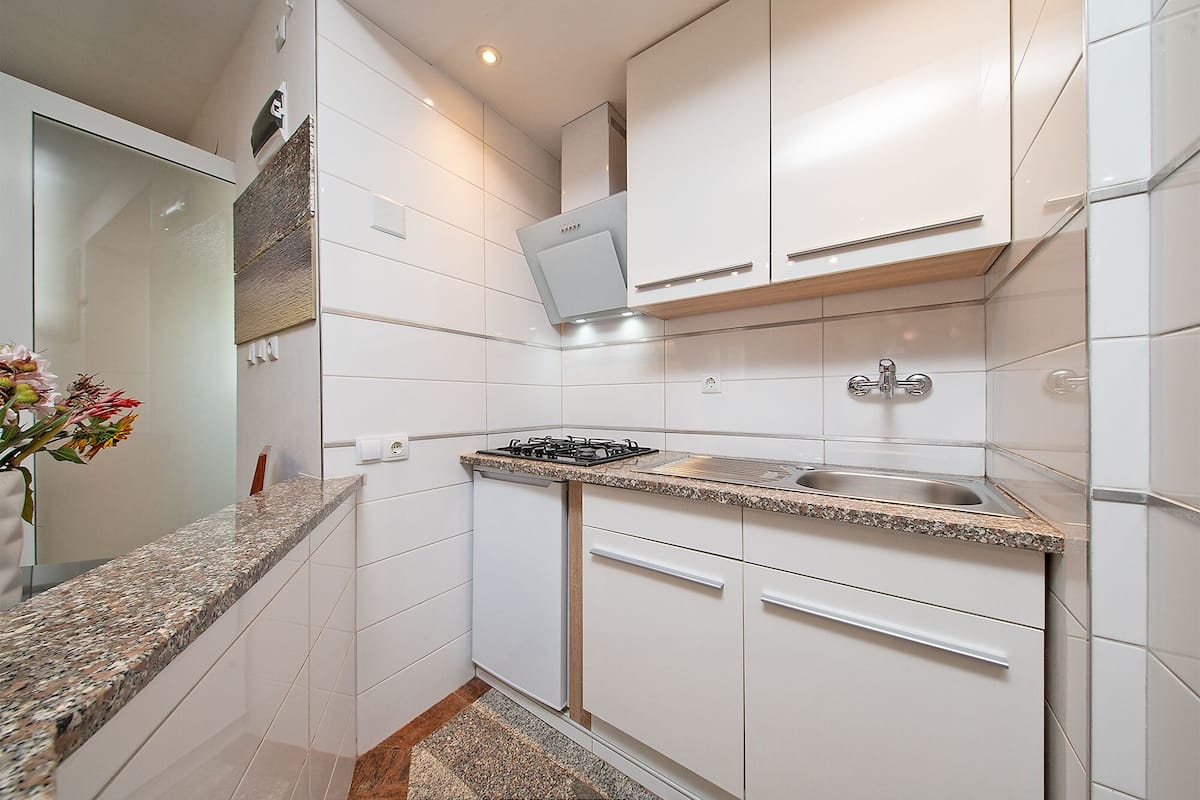 Una cocina moderna con armarios blancos, encimera de granito, pileta de acero inoxidable y estufa a gas.