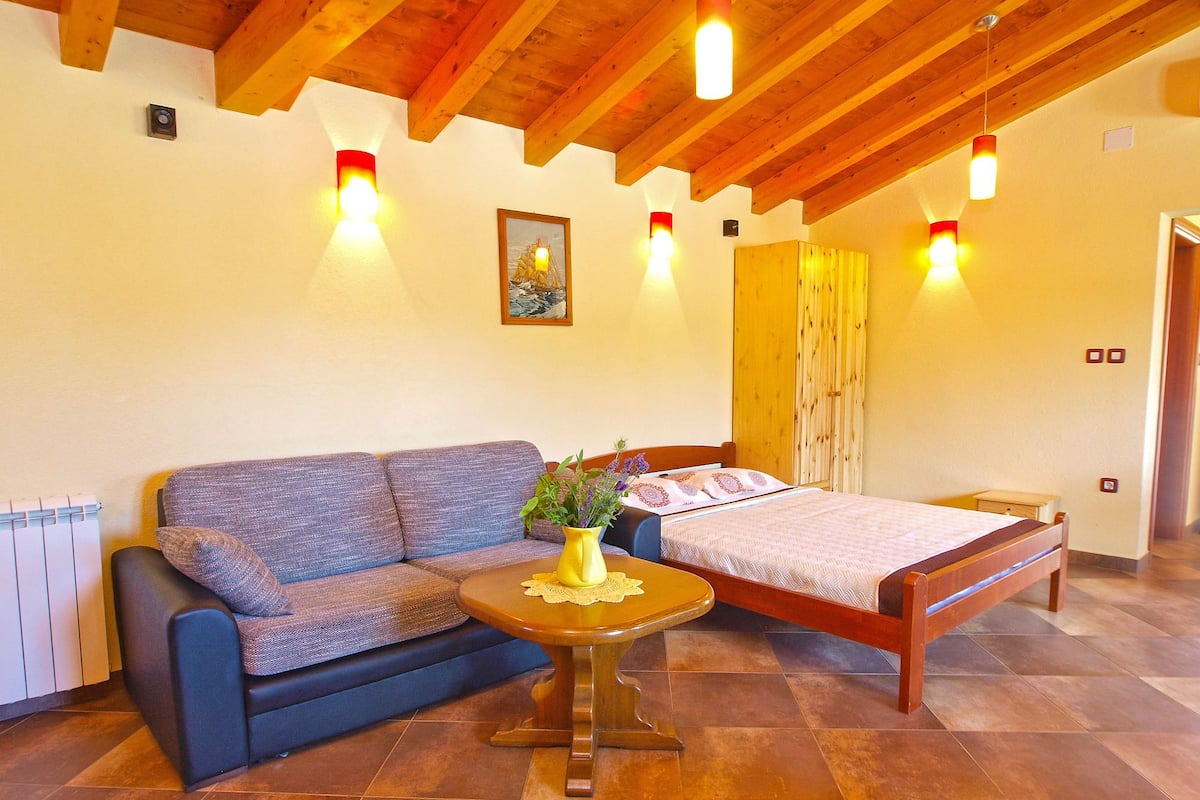 Una habitación con techo de madera, una cama, un sofá, una mesita con un florero y un radiador.