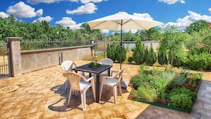 An outdoor patio with a table and chairs, surrounded by greenery and a clear blue sky. - Apartment Tatjana 411 (Medulin)