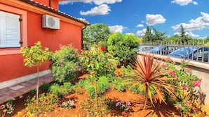 A red building with a garden in front, a blue car, and a clear sky. - Apartment Tatjana 411 (Medulin)