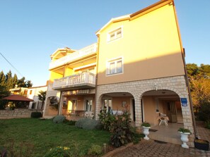 A two-story building with a balcony, a stone facade, and a well-maintained garden.