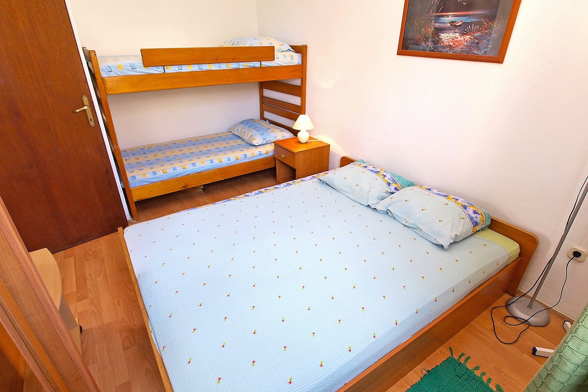 Een slaapkamer met een stapelbed, een enkel bed, een nachtkastje met een lamp en een schilderij aan de muur.
