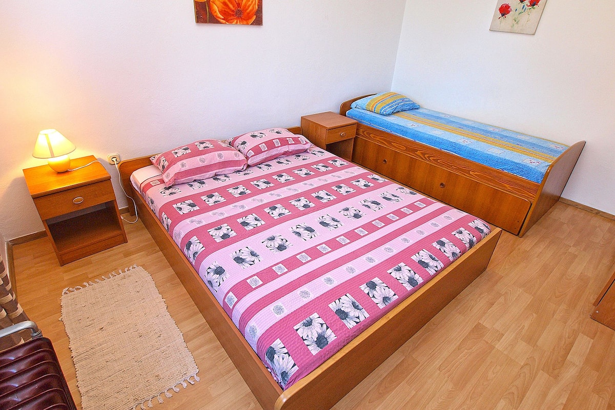 Een slaapkamer met een houten bed, een nachtkastje met een lamp, een klein bijzettafeltje en een vloerkleed.
