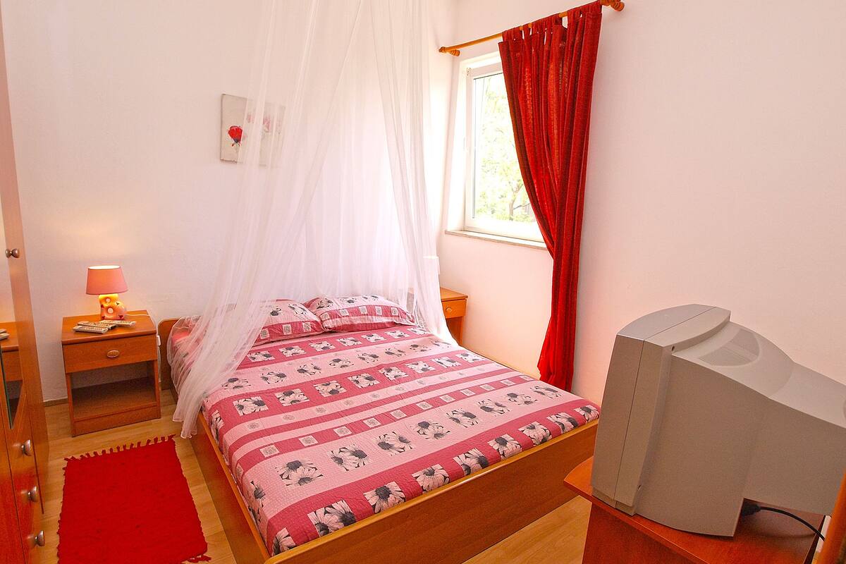 Een slaapkamer met een bed, een nachtkastje met een lamp, een tv-meubel en een raam met gordijnen.
