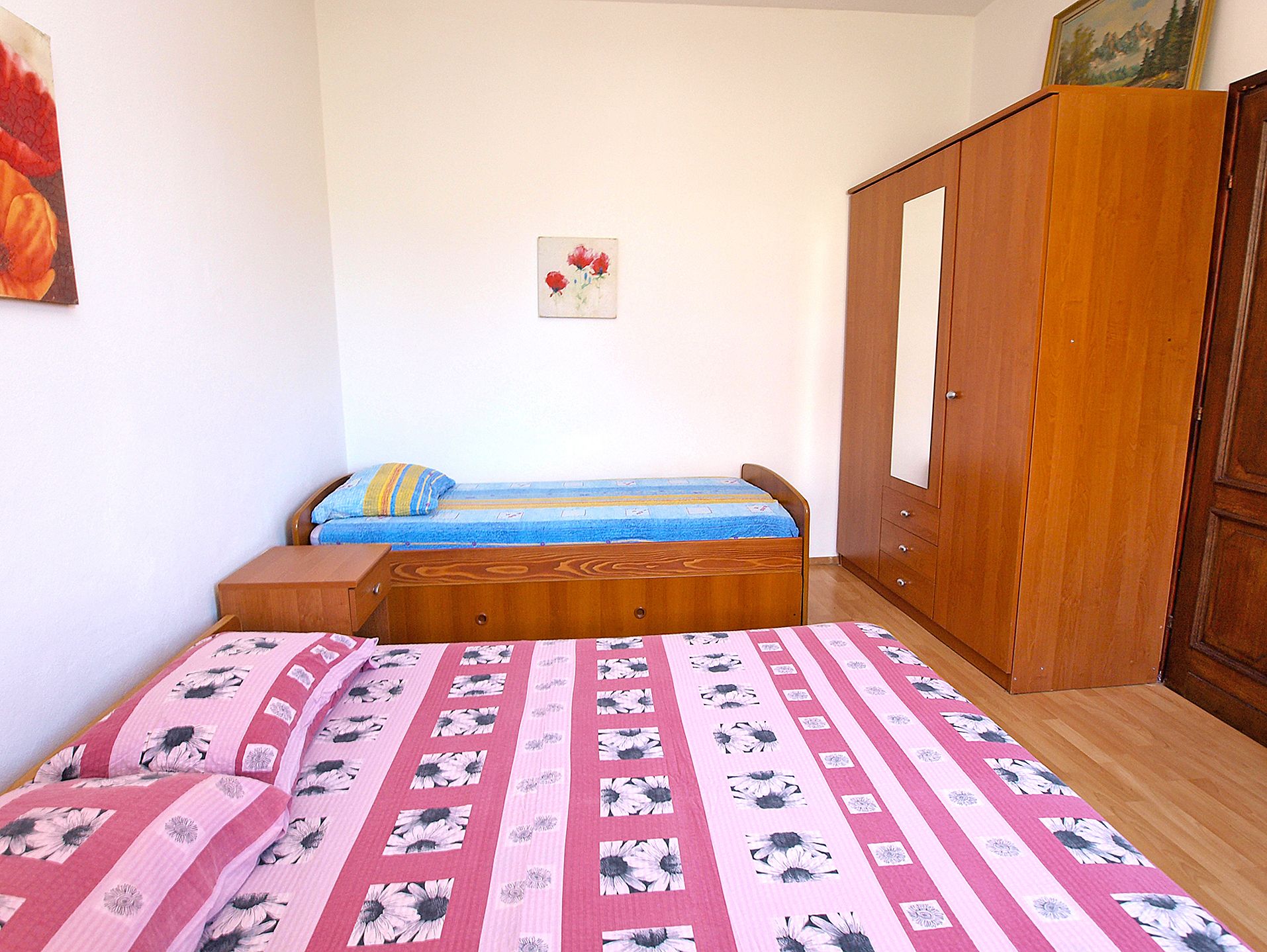 Een slaapkamer met een bed, een houten garderobe en een klein nachtkastje.