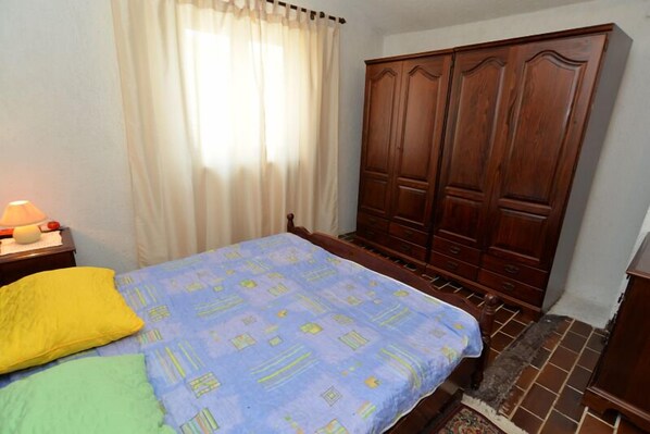 A bedroom with a bed, a nightstand, a lamp, a wardrobe, and a window with curtains.