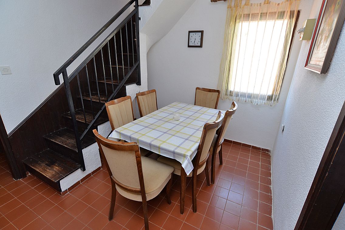 A dining area with a table set for four, a staircase with black railings, and a window with curtains.