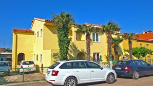 A yellow building with a red-tiled roof, parked cars, and palm trees. - Apartment Gey 671 (Medulin)