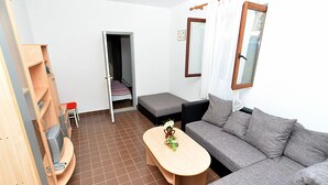 A compact living space with a sofa, a small table, a television, and a bookshelf. - Apartment Gey 671 (Medulin)