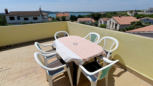 A balcony with a table and chairs, overlooking a coastal town with houses and a body of water. - Apartment Gey 671 (Medulin)