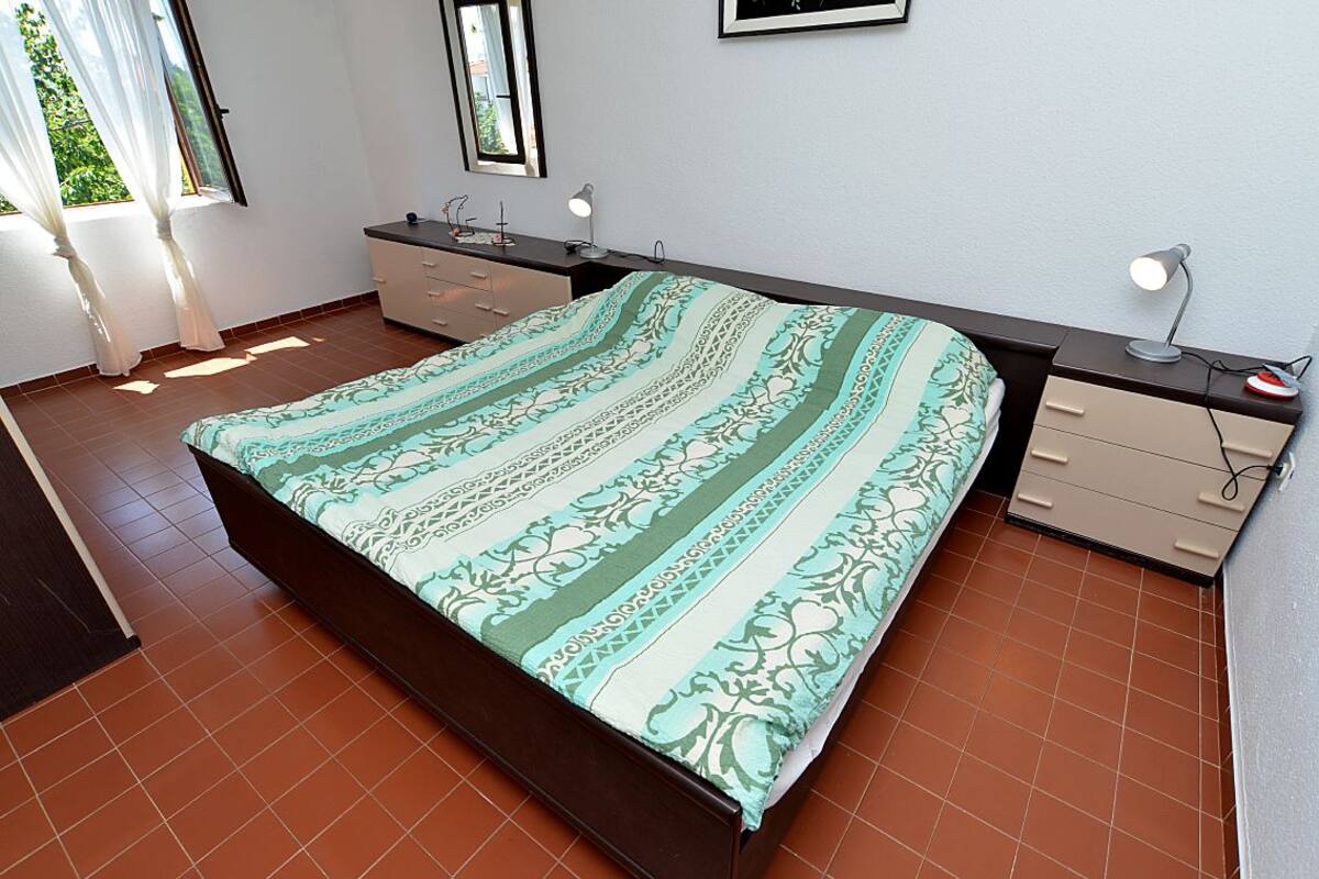 A bedroom with a bed, a desk, a chair, a dresser, and a window with curtains.