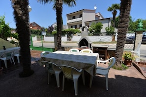 An outdoor patio with a table and chairs, a stone oven, and a fenced area with a building in the background. - Apartment Gey 671 (Medulin)