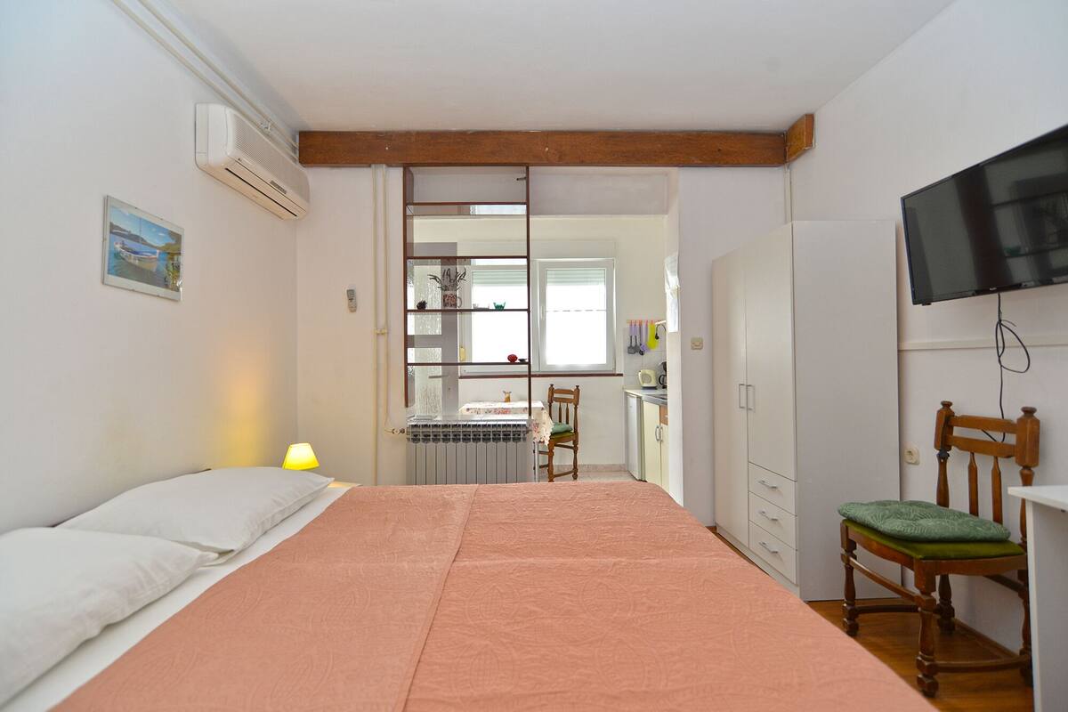 Quarto com cama, cadeira, escrivaninha, espelho, radiador e televisão.