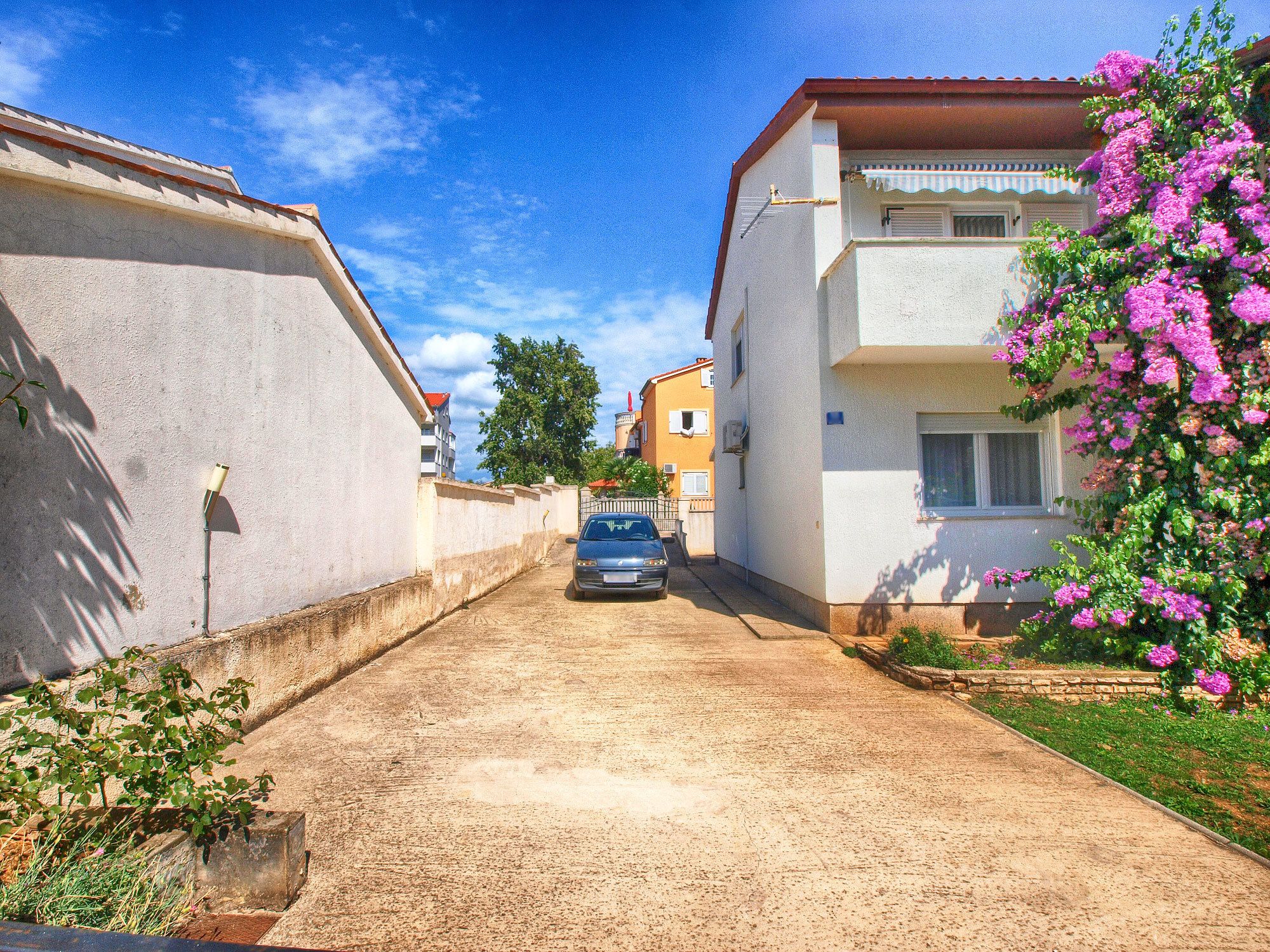 Une rue étroite, avec une voiture garée, des bâtiments de chaque côté et un ciel dégagé.