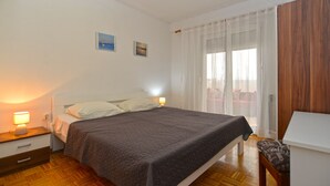 Un dormitorio con cama, lámparas de noche, una mesita de noche de madera, una silla y una ventana con cortinas de encaje.