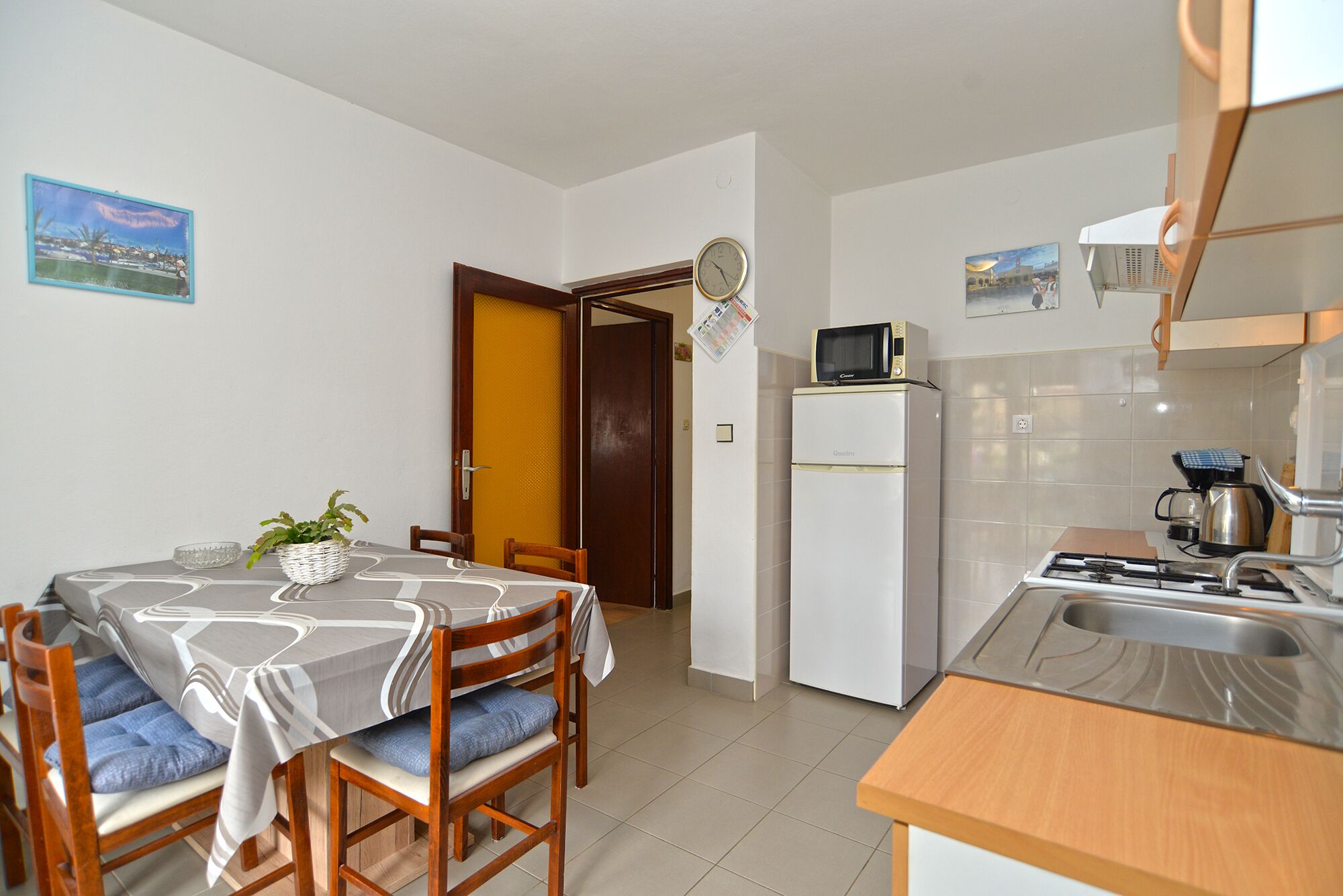 A compact kitchen with a refrigerator, microwave, and stove. There is a dining table with chairs and a potted plant.