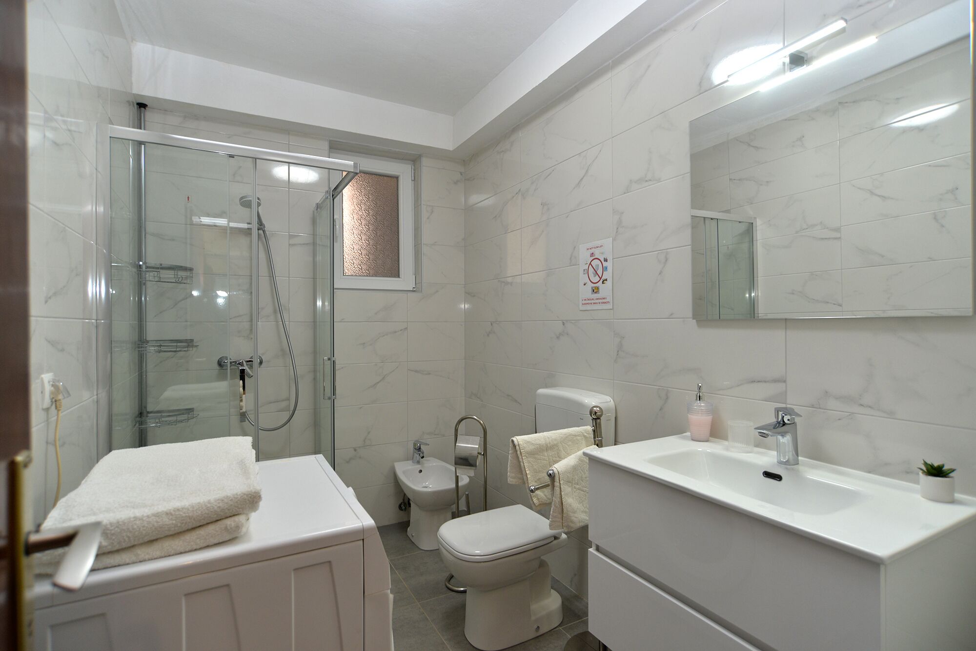 A modern bathroom with a glass shower enclosure, a toilet, and a sink with a mirror above it.