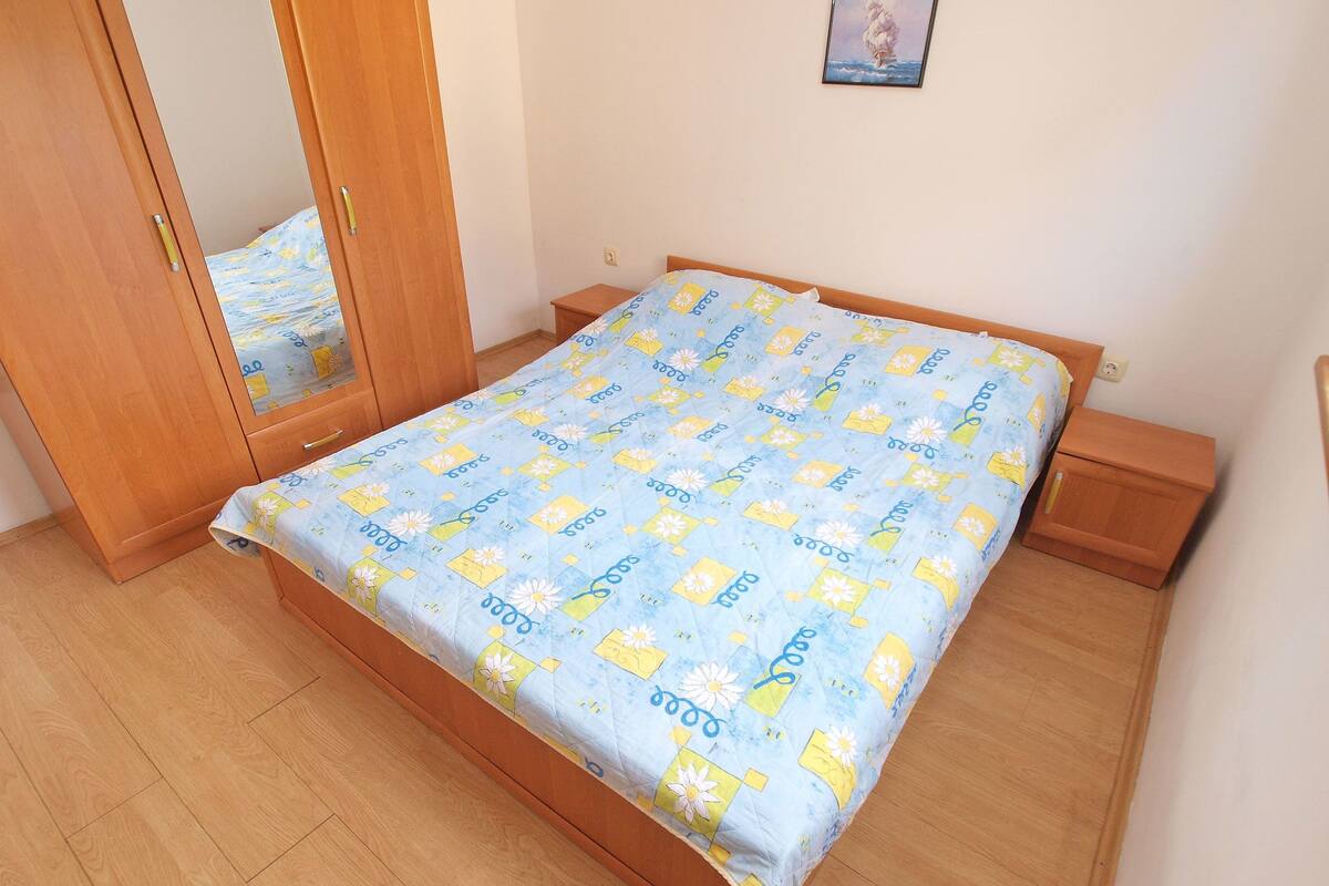 A bedroom with a wooden bed, a nightstand, a wardrobe, and a mirror.