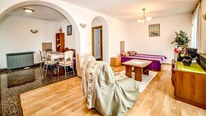 A spacious living room with a wooden floor, a sofa, a dining table with chairs, and a kitchen area with a radiator. - Apartment Ivanka 378 (Rovinj)