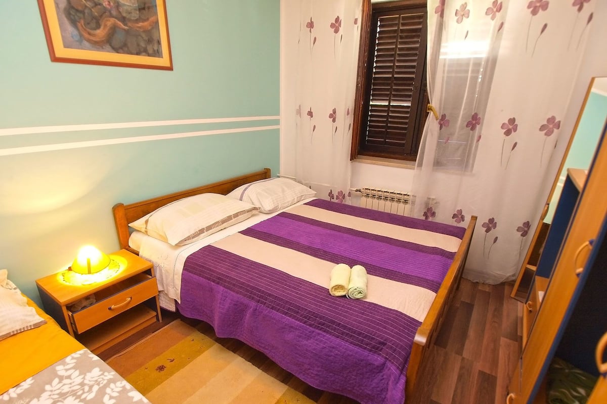 Um quarto com uma cama, uma mesinha de cabeceira, persianas e um espelho.
