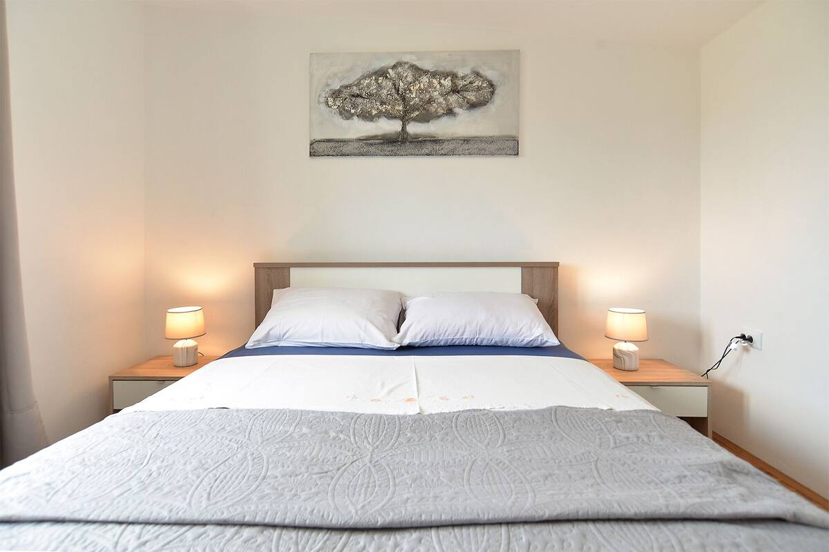 A neatly made bed with a white and blue bedspread, two white pillows, and two bedside lamps on wooden nightstands.