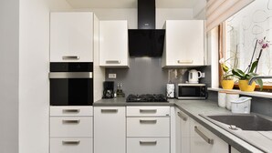 Una cocina moderna con armarios blancos, una campana extractora negra, un microondas, una estufa a gas y una ventana con plantas.