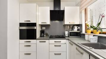 A modern kitchen with white cabinets, a black range hood, a microwave, a gas stove, and a window with plants.