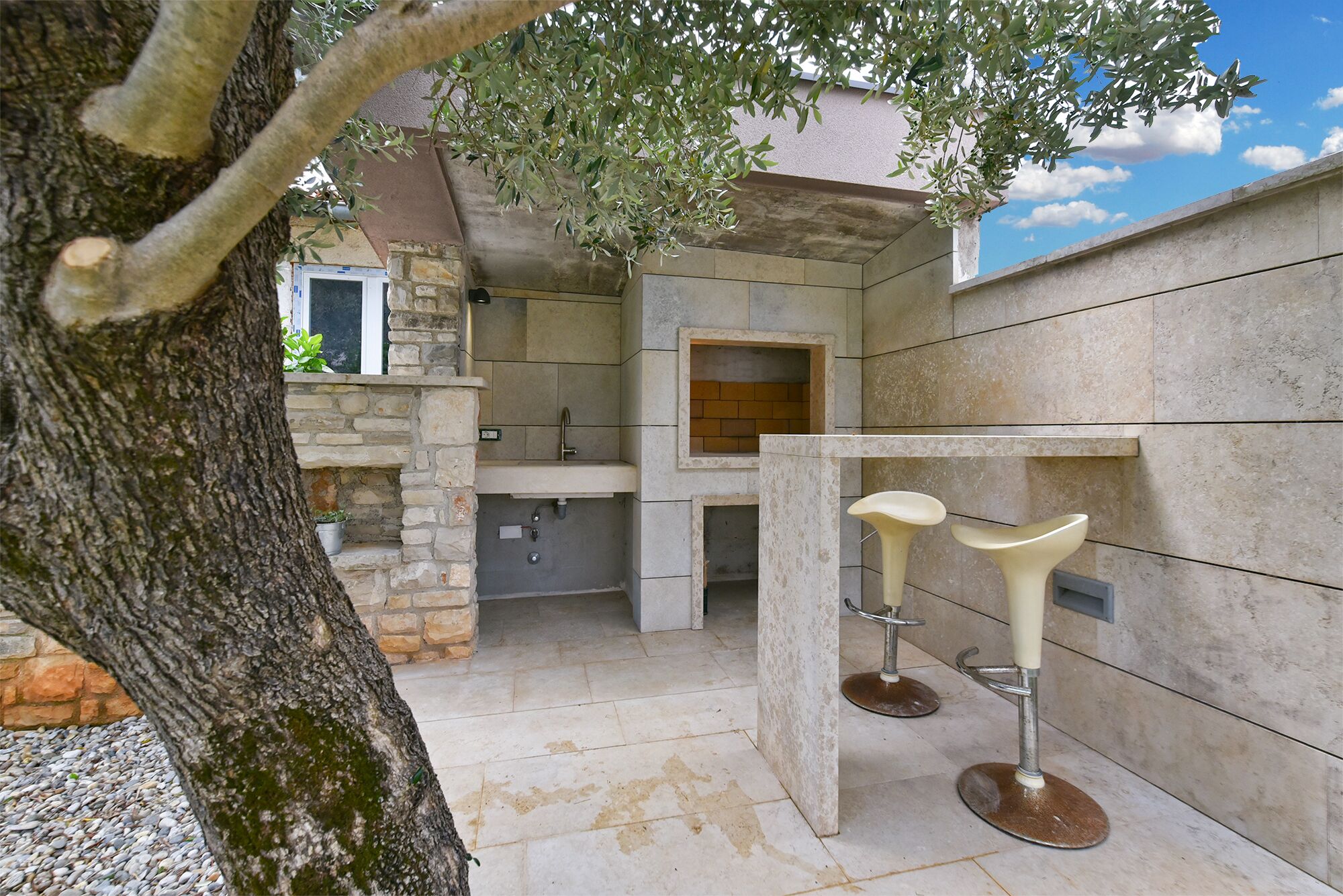 An outdoor kitchen area with stone walls, a built-in oven, and two bar stools.
