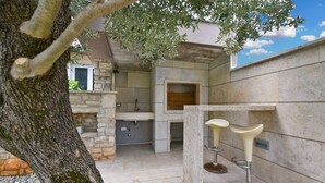 Un área de cocina al aire libre con paredes de piedra, horno empotrado y dos taburetes de bar.