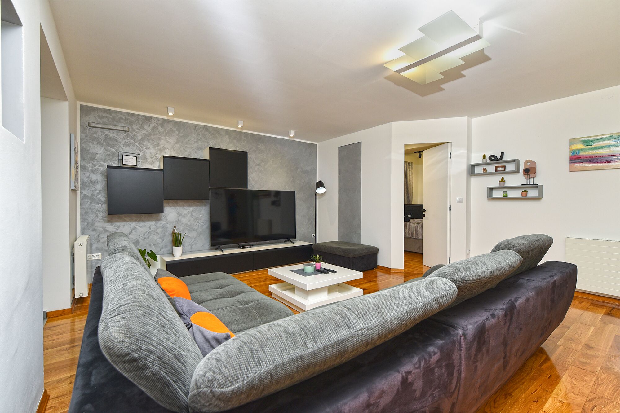 Una sala de estar moderna con un televisor de pantalla plana grande, sofás grises, una mesa de centro y un diseño minimalista.