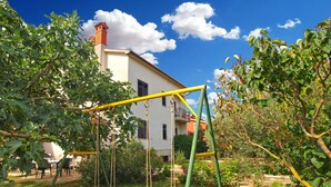 A garden with a swing set, a white building with a red roof, and a clear blue sky. - Apartment Milka 442 (Fazana)