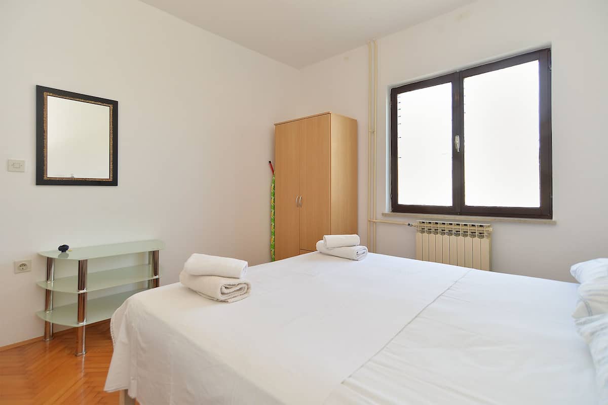 Quarto com cama, guarda-roupa, espelho e janela.
