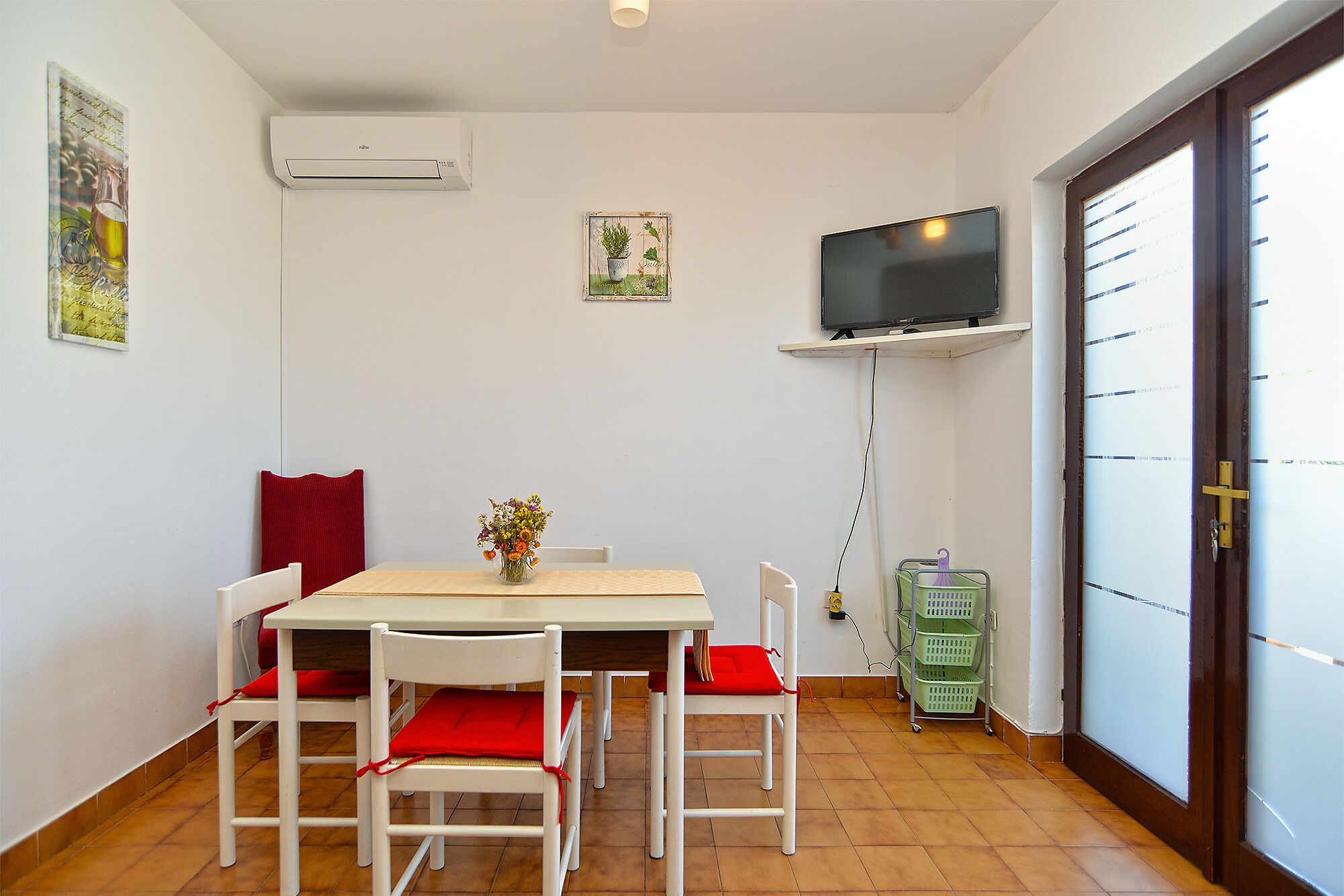Un comedor con una mesa y sillas, un televisor montado en la pared y una puerta con ventanal.