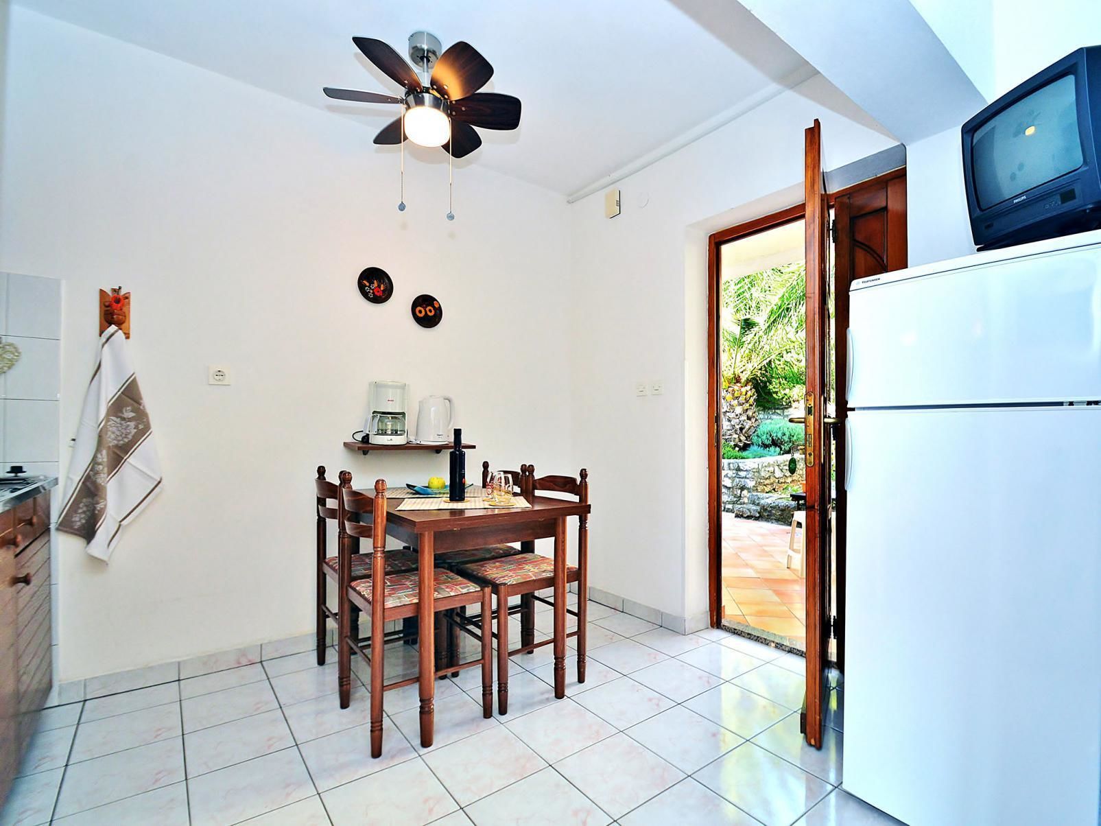Une cuisine équipée d’une table à manger, de chaises, d’un ventilateur de plafond, d’un réfrigérateur et d’un téléviseur.