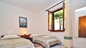 Ein Zimmer mit zwei Betten, einem Vorhangfenster, einer Tür und einem Bild an der Wand.