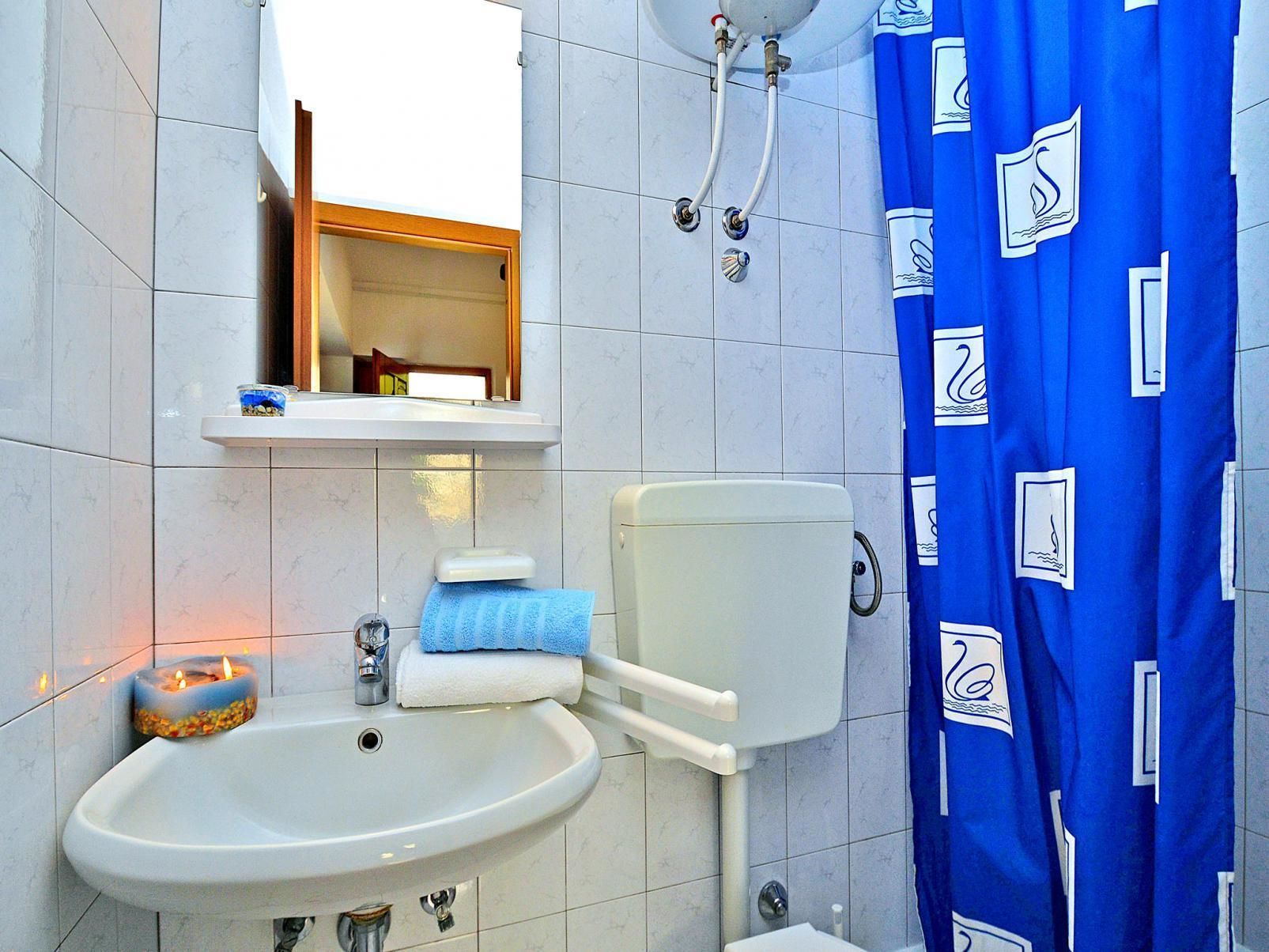 Un baño con un lavabo blanco, un inodoro, una cortina de ducha azul y un espejo sobre el lavabo.