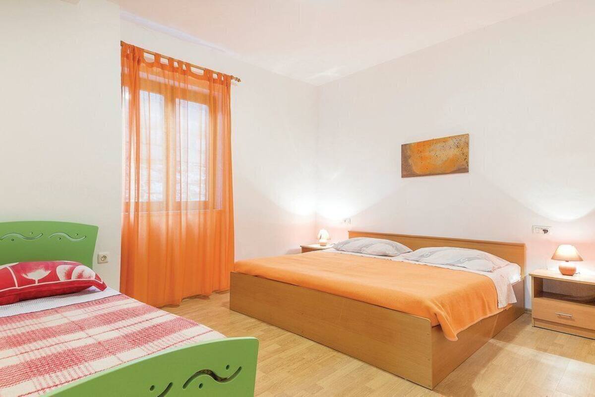 A bedroom with a wooden bed, two bedside tables with lamps, a green chair, and a window with orange curtains.