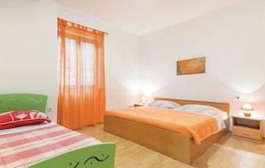 Um quarto com uma cama de madeira, duas mesas de cabeceira com abajures, uma cadeira verde e uma janela com cortinas laranja.