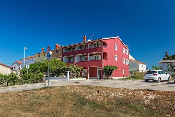 A red multi-story residential building with balconies, a stop sign, and a white car parked in front. - Apartment Boris 771 (Fazana)